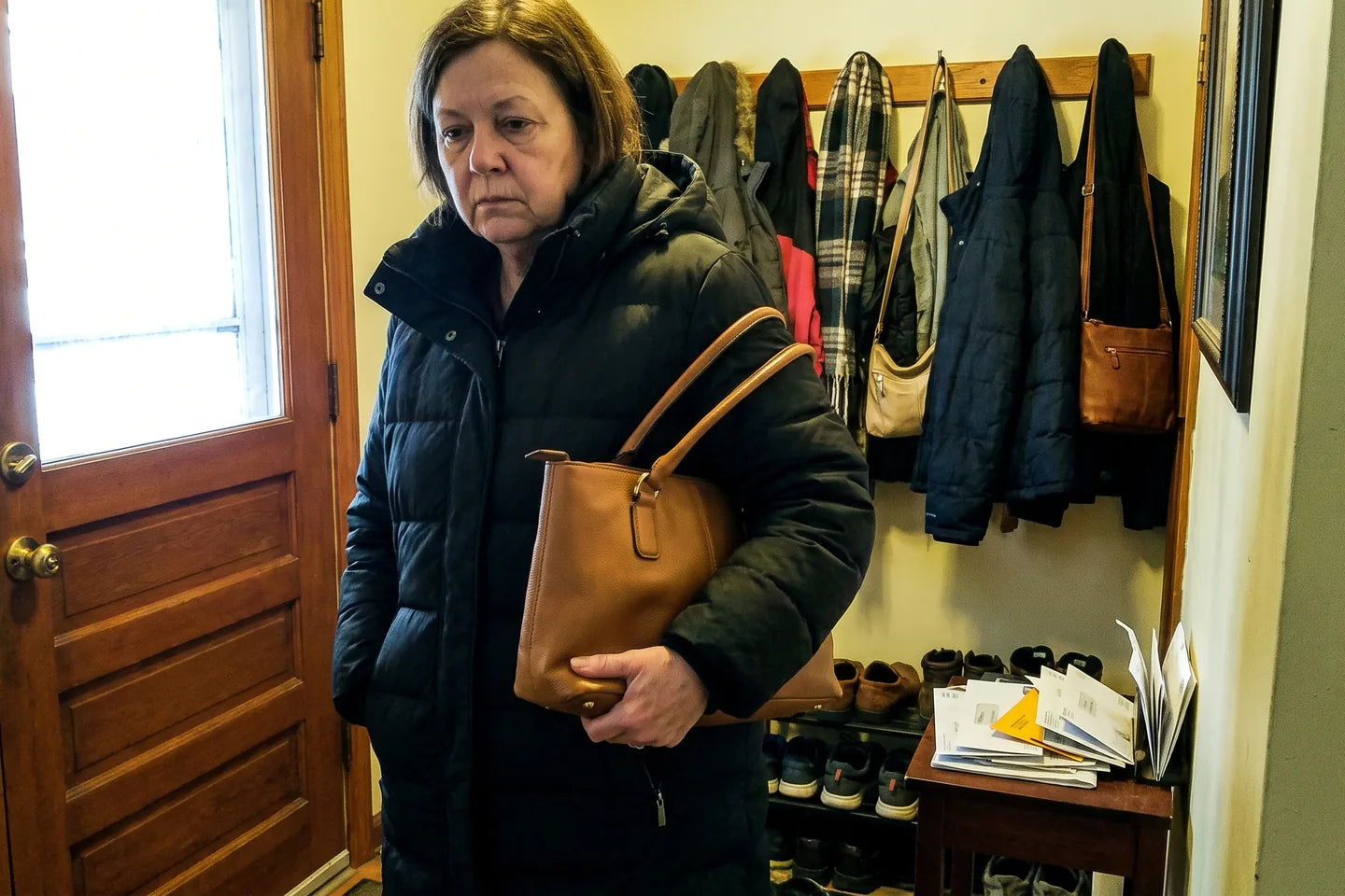 A woman in a heavy winter coat carrying a leather bag along her forearm, the strap plainly too short to clear the coat.