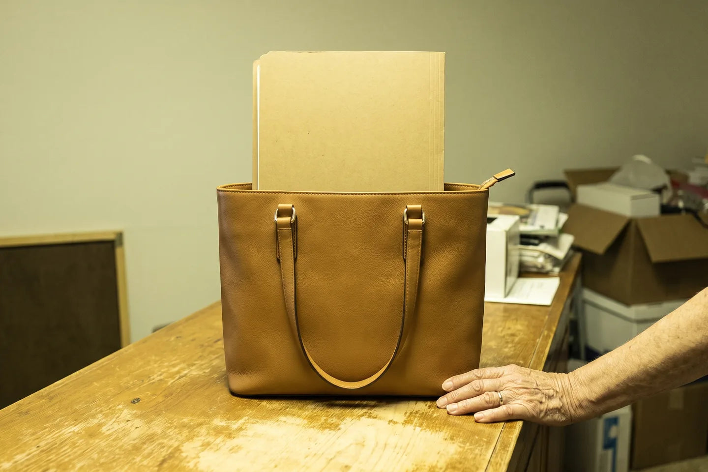 A leather tote standing upright and unaided on a counter with a folder standing square inside it.
