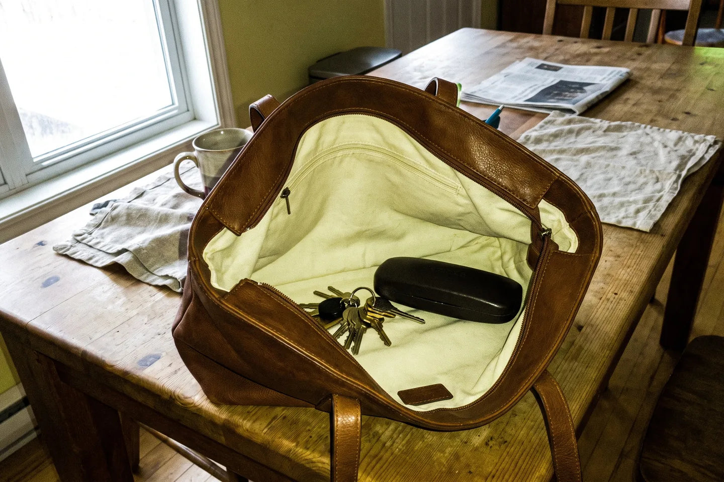 A bag open on a table, the pale interior clearly visible, keys and a glasses case in plain sight against the light lining.