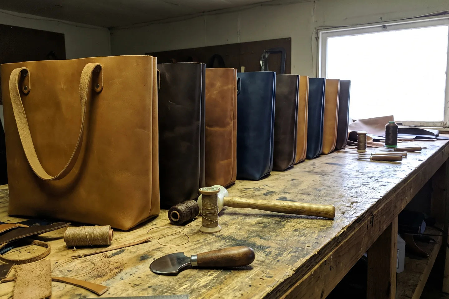 Finished bags standing shoulder to shoulder along the workbench, tools and offcuts in frame.